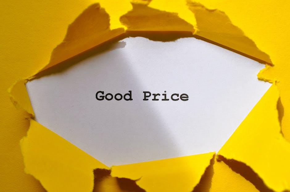 A close-up view of a torn yellow paper with jagged edges revealing a white piece of paper underneath, on which the words 'Good Price' are printed in black text. The torn yellow paper appears to be part of packaging or wrapping material, possibly related to the moving or packing process. The background behind the torn paper is also yellow, and the lighting highlights the texture and imperfections of the torn edges. This image relates to home relocation, packing, and moving logistics involving packaging materials used by [COMPANY_NAME], such as in loading procedures or transport preparations during a house move.